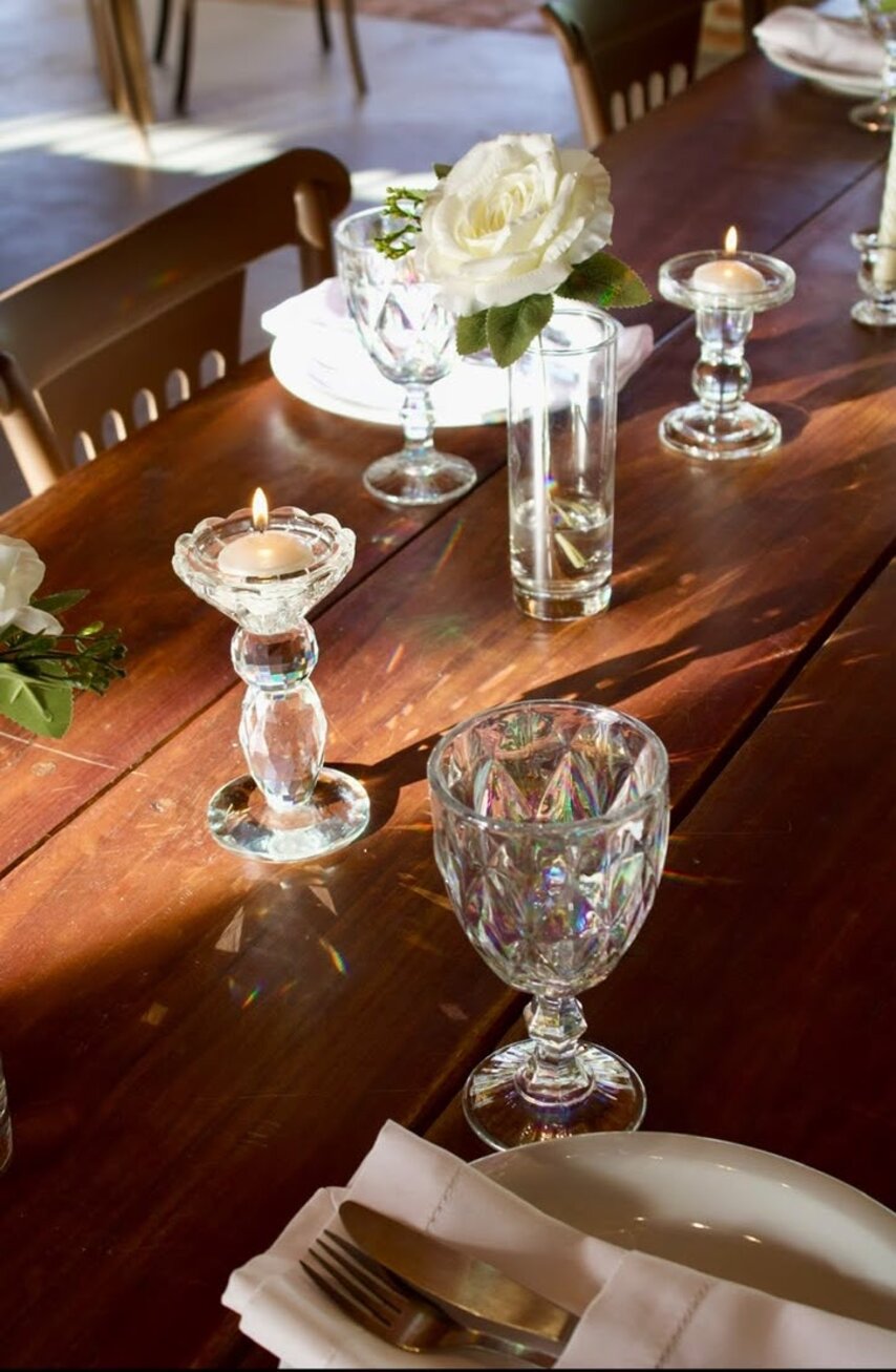 Mise en place em madeira — Rosa branca, castiçais de cristal e guardanapo de linho sobre a madeira crua.