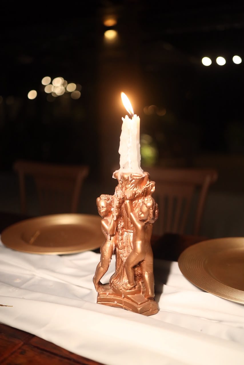 Castiçal dourado esculpido — Peça em dourado envelhecido com vela alta, sobre pratos rasos e caminho de linho.